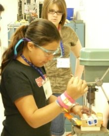 A photo of 2 girls using a drill press.